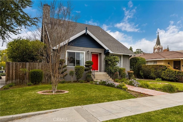 view of front of house with stucco siding, a shingled roof, a front lawn, and fence