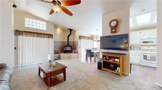 living area featuring visible vents, light carpet, ceiling fan with notable chandelier, a wood stove, and high vaulted ceiling