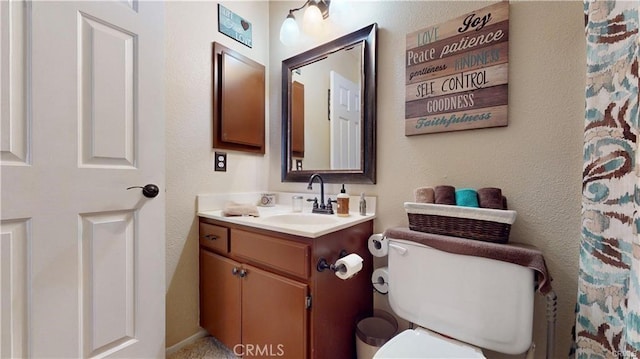 bathroom with vanity, toilet, and a textured wall