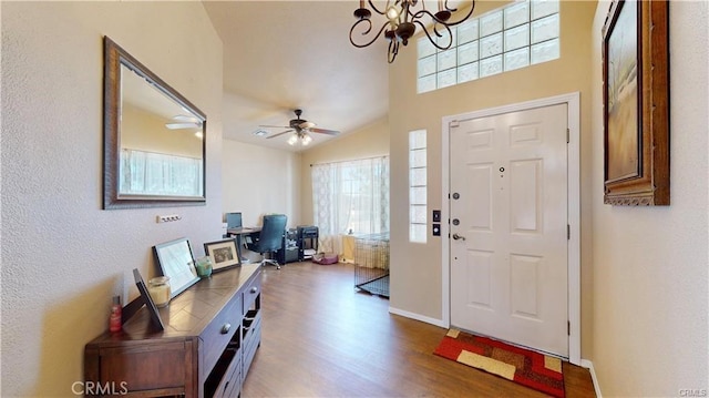 entryway featuring plenty of natural light, ceiling fan with notable chandelier, baseboards, and wood finished floors