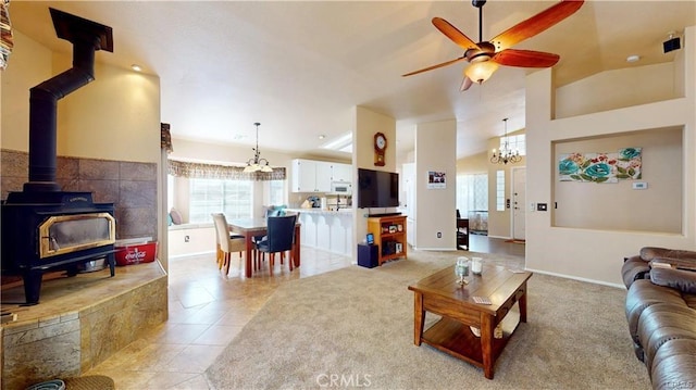 living area featuring light tile patterned floors, baseboards, lofted ceiling, a wood stove, and ceiling fan with notable chandelier