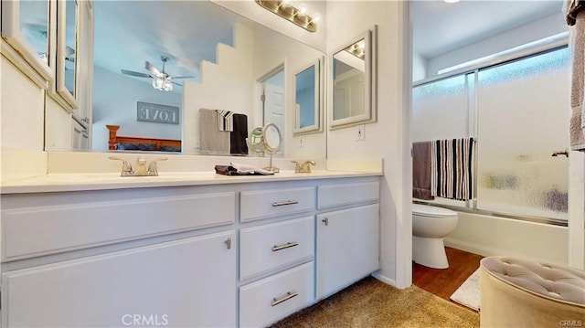 bathroom with toilet, a ceiling fan, a sink, shower / bath combination with glass door, and double vanity