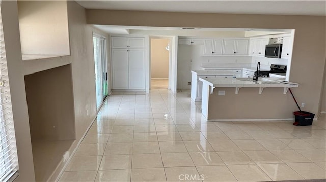 kitchen featuring light tile patterned flooring, appliances with stainless steel finishes, a peninsula, and white cabinets