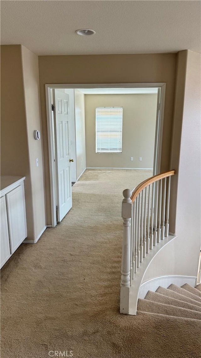 hall with an upstairs landing, carpet, baseboards, and a textured ceiling