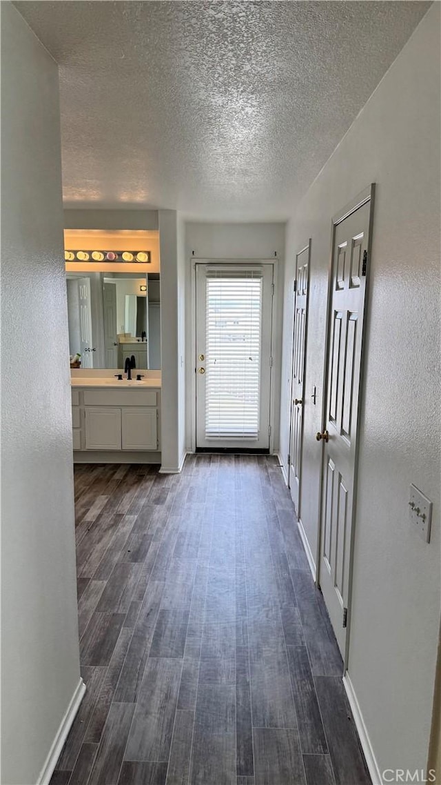 hallway with a textured ceiling, dark wood-type flooring, and baseboards