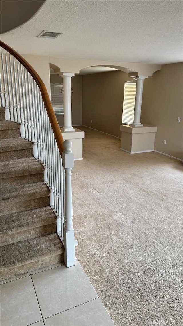 stairs with a textured ceiling, carpet flooring, and ornate columns