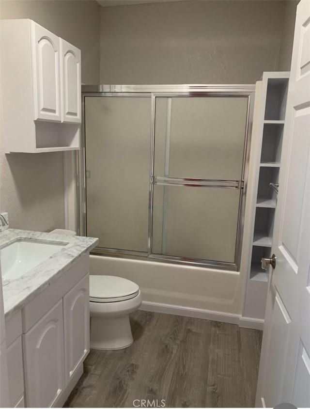 bathroom featuring bath / shower combo with glass door, toilet, vanity, and wood finished floors