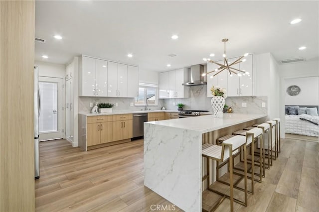 kitchen with modern cabinets, light wood-style flooring, stainless steel appliances, a peninsula, and wall chimney exhaust hood