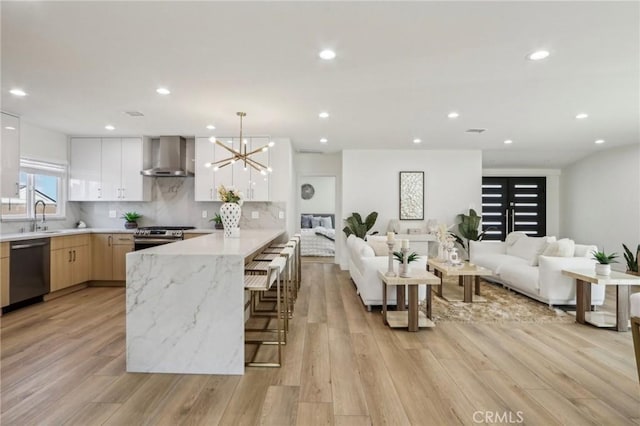 kitchen featuring a sink, open floor plan, a peninsula, appliances with stainless steel finishes, and wall chimney range hood