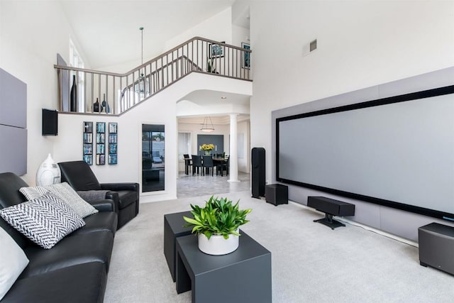 carpeted home theater room with visible vents, a high ceiling, and ornate columns