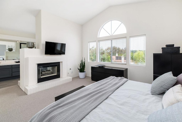 bedroom featuring a glass covered fireplace, lofted ceiling, carpet, and ensuite bath