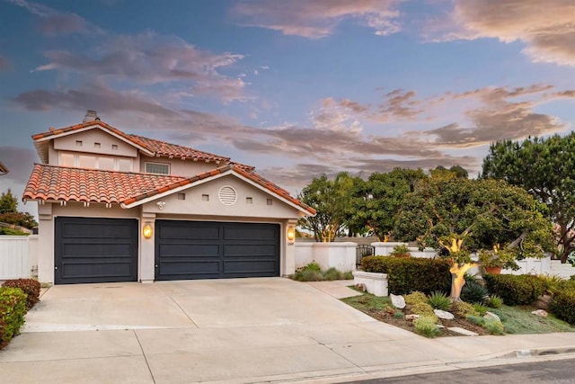 mediterranean / spanish house with a tile roof, concrete driveway, a garage, and fence