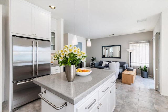 kitchen featuring stainless steel built in fridge, a kitchen island, open floor plan, white cabinets, and light stone countertops