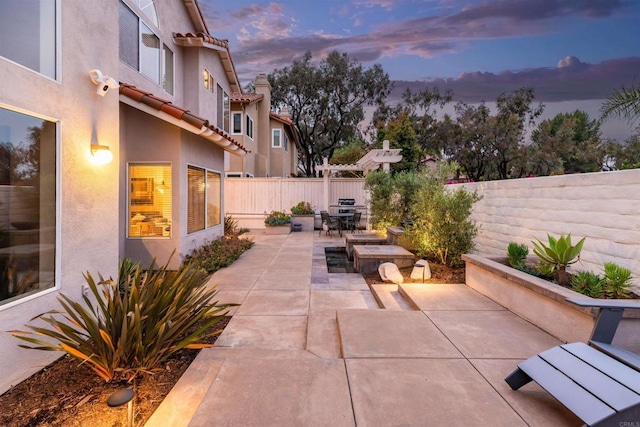 patio terrace at dusk featuring a fenced backyard