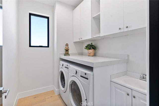 clothes washing area featuring baseboards, washing machine and dryer, light wood-style floors, cabinet space, and a sink