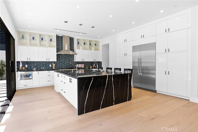 5012 Enfield Ave, Encino, CA 91316 - kitchen featuring stainless steel appliances, wall chimney exhaust hood, dark countertops, light wood finished floors, and a large island with sink