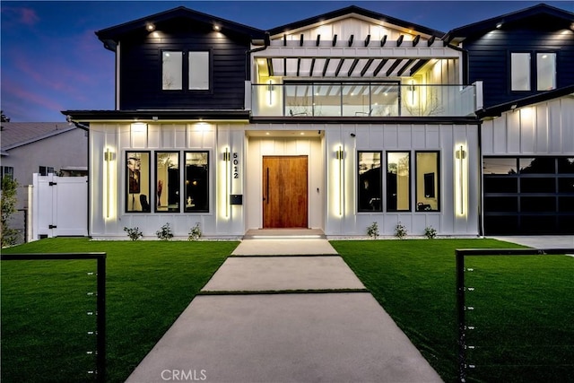 modern farmhouse style home featuring board and batten siding, a front yard, a balcony, and fence