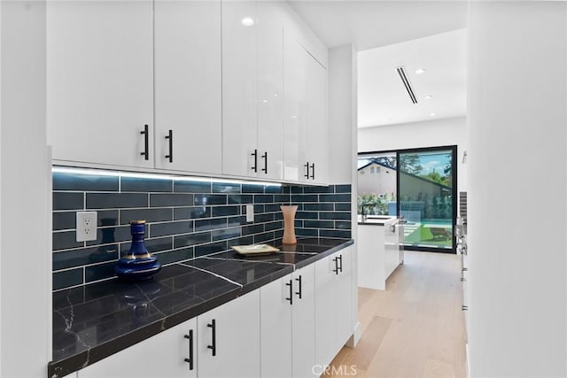 kitchen with dark countertops, light wood-type flooring, decorative backsplash, white cabinets, and modern cabinets