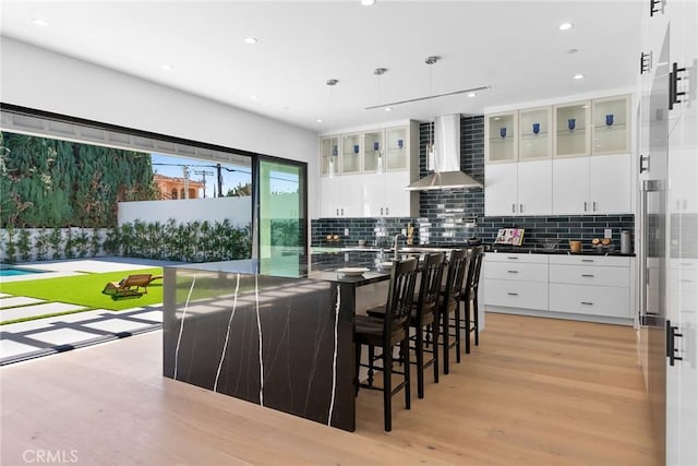 kitchen with dark countertops, tasteful backsplash, light wood-type flooring, and wall chimney range hood