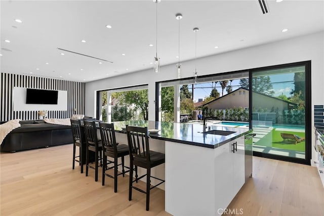 kitchen with modern cabinets, light wood-style flooring, a sink, dark countertops, and a large island with sink