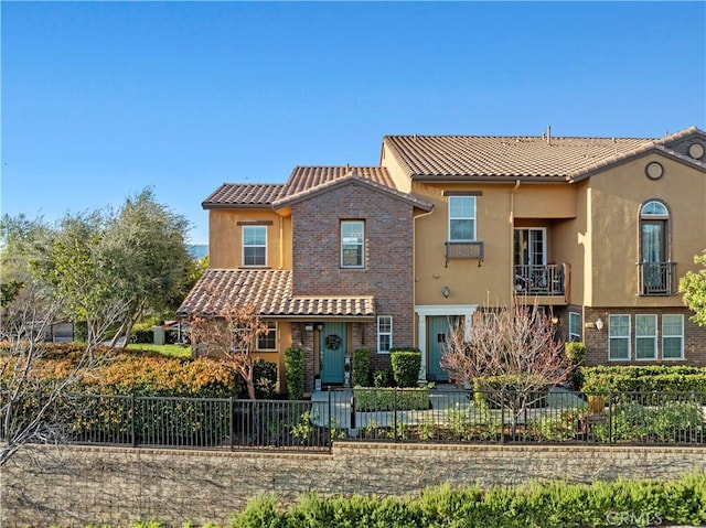 view of front facade with a fenced front yard, brick siding, stucco siding, and a tile roof