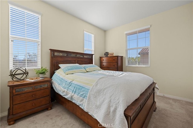 bedroom with multiple windows, light colored carpet, and baseboards