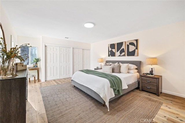 bedroom with baseboards, two closets, and light wood finished floors