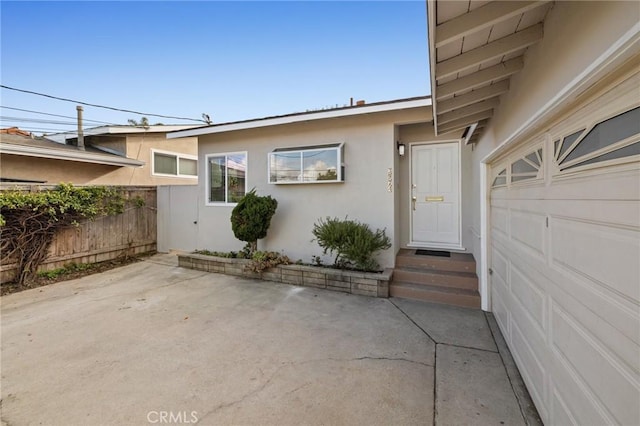 doorway to property featuring fence, a garage, driveway, and stucco siding