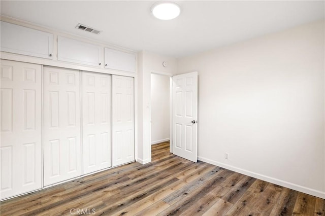 unfurnished bedroom with visible vents, baseboards, a closet, and wood finished floors