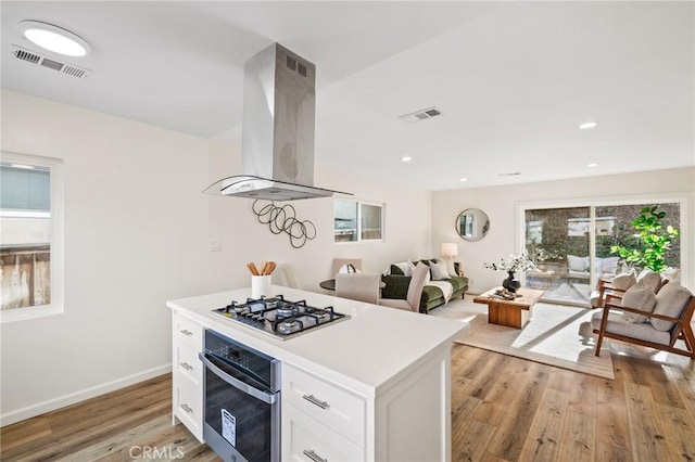 kitchen featuring light wood finished floors, visible vents, extractor fan, white cabinets, and stainless steel appliances