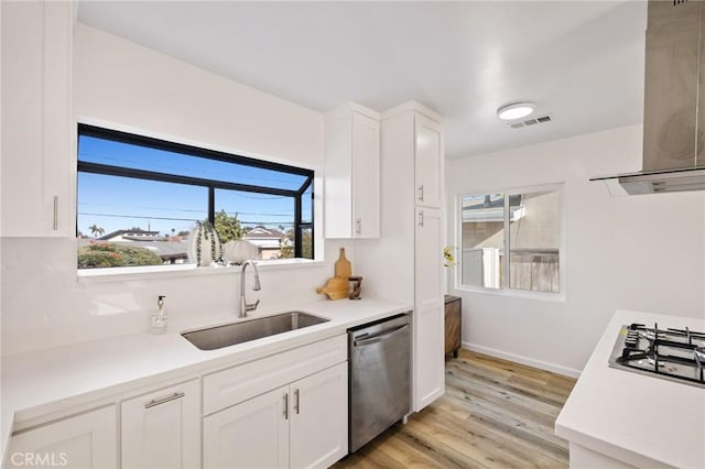 kitchen featuring visible vents, a sink, stainless steel appliances, wall chimney exhaust hood, and light countertops