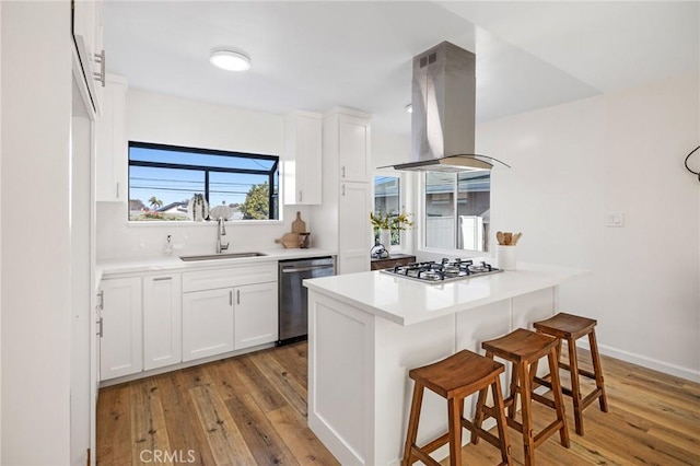 kitchen with a breakfast bar, stainless steel appliances, island range hood, white cabinetry, and a sink