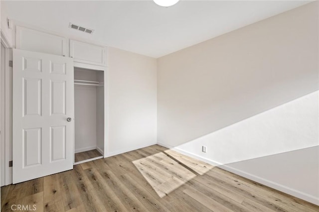 unfurnished bedroom featuring visible vents, baseboards, a closet, and wood finished floors