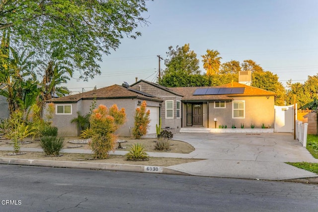 ranch-style house featuring stucco siding, driveway, roof mounted solar panels, fence, and an attached garage