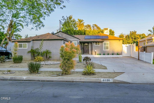 ranch-style home with stucco siding, roof mounted solar panels, driveway, and fence