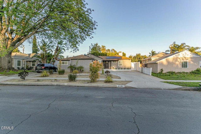 view of front of property with stucco siding, solar panels, concrete driveway, and fence