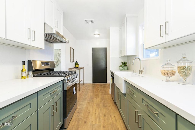 kitchen featuring stainless steel gas range oven, visible vents, green cabinets, under cabinet range hood, and a sink