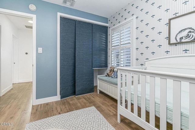 bedroom with wood finished floors, visible vents, a closet, and baseboards