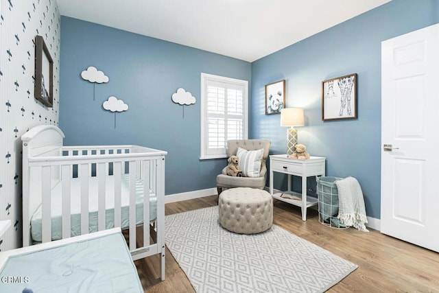 bedroom with a nursery area, baseboards, and wood finished floors