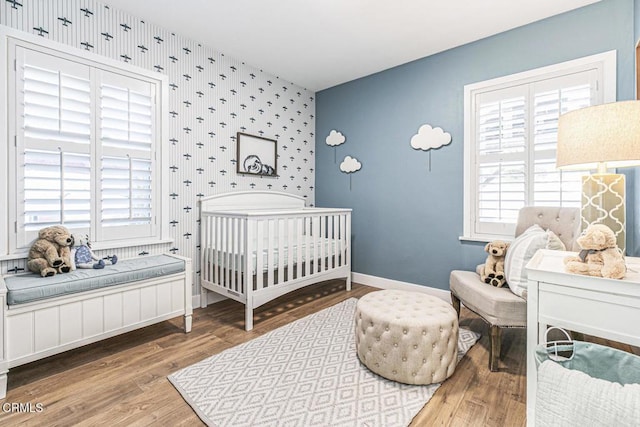 bedroom with baseboards, wood finished floors, an accent wall, and wallpapered walls