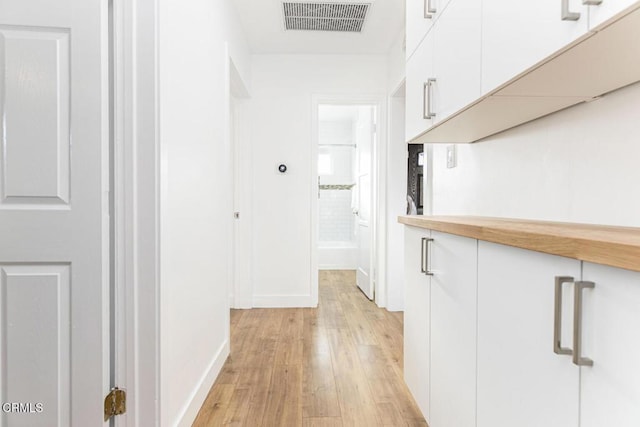 hall featuring baseboards, visible vents, and light wood finished floors