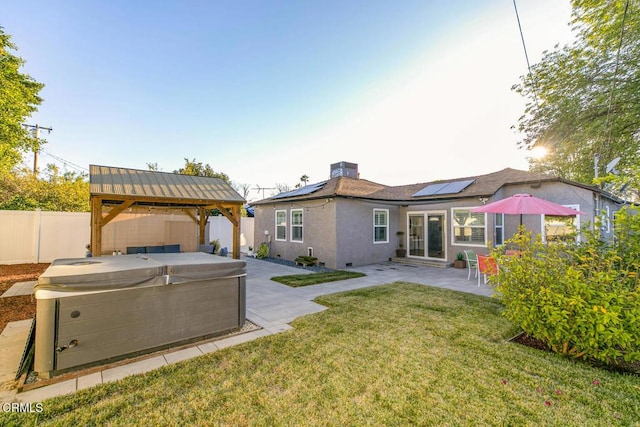 back of house featuring roof mounted solar panels, a patio, a fenced backyard, a gazebo, and a hot tub