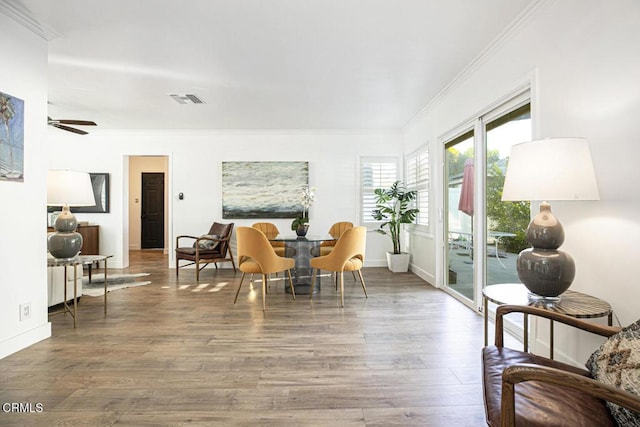 dining space featuring wood finished floors, baseboards, visible vents, ceiling fan, and crown molding