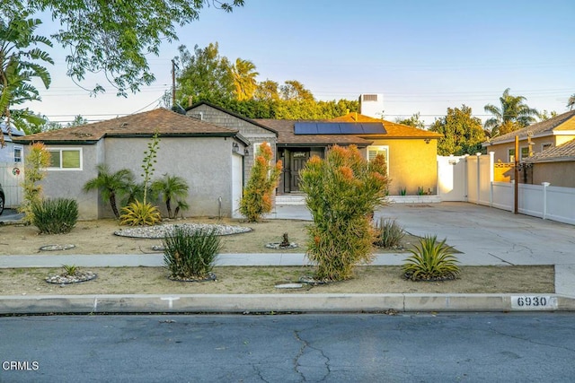 view of front facade featuring fence, driveway, stucco siding, a garage, and roof mounted solar panels