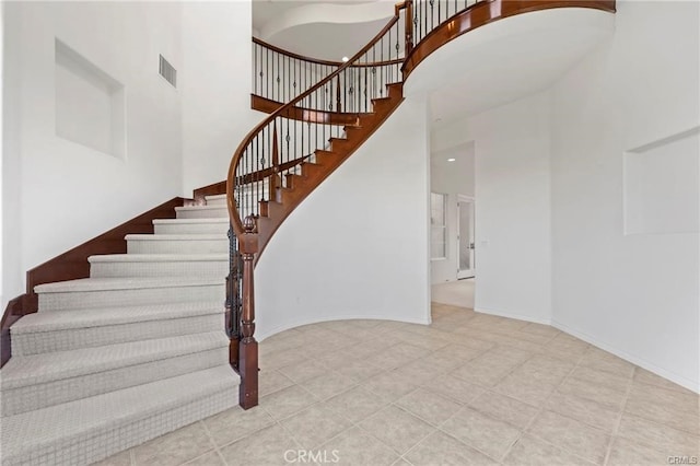 stairway with baseboards, visible vents, and a towering ceiling