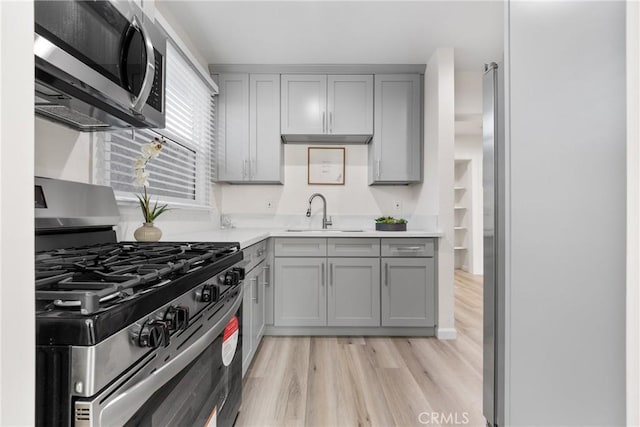 kitchen with light wood-type flooring, gray cabinets, a sink, stainless steel appliances, and light countertops