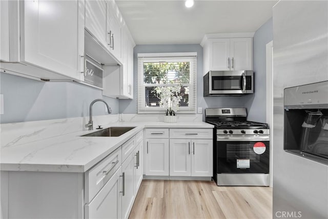 kitchen with light stone counters, a sink, stainless steel appliances, white cabinets, and light wood-type flooring