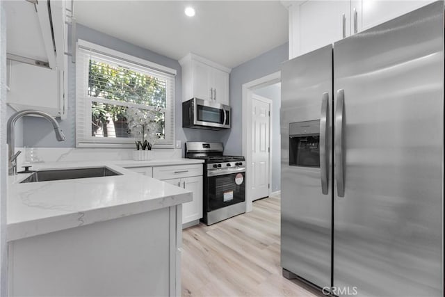 kitchen featuring light stone countertops, light wood finished floors, a sink, stainless steel appliances, and white cabinets