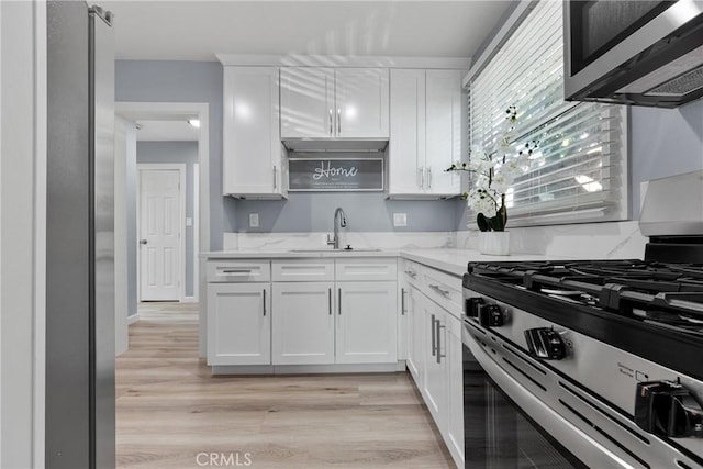 kitchen with light wood-type flooring, a sink, light stone counters, stainless steel appliances, and white cabinets