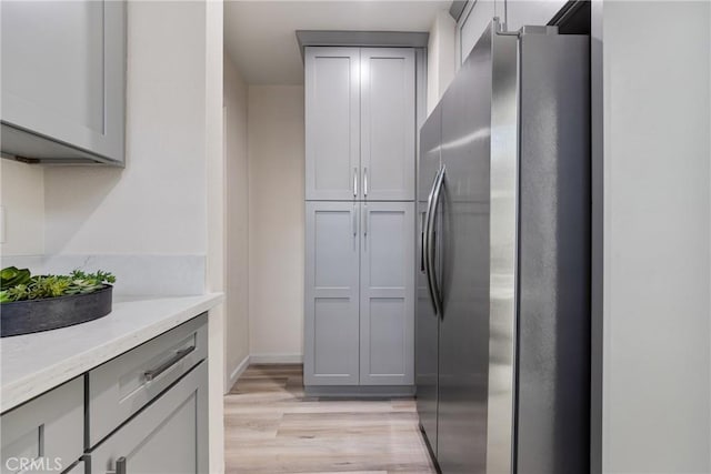 kitchen with light wood-style flooring, stainless steel fridge, gray cabinets, and light countertops